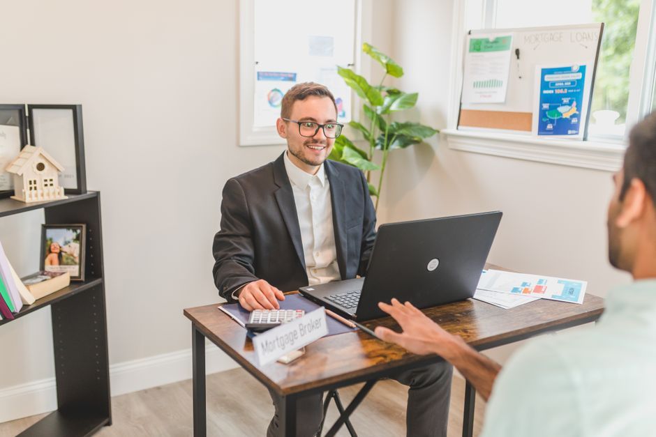 Mortgage broker meeting a client across a desk with a laptop and calculator