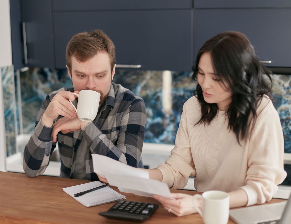 Couple reviewing paperwork with a calculator and notebook at a kitchen table