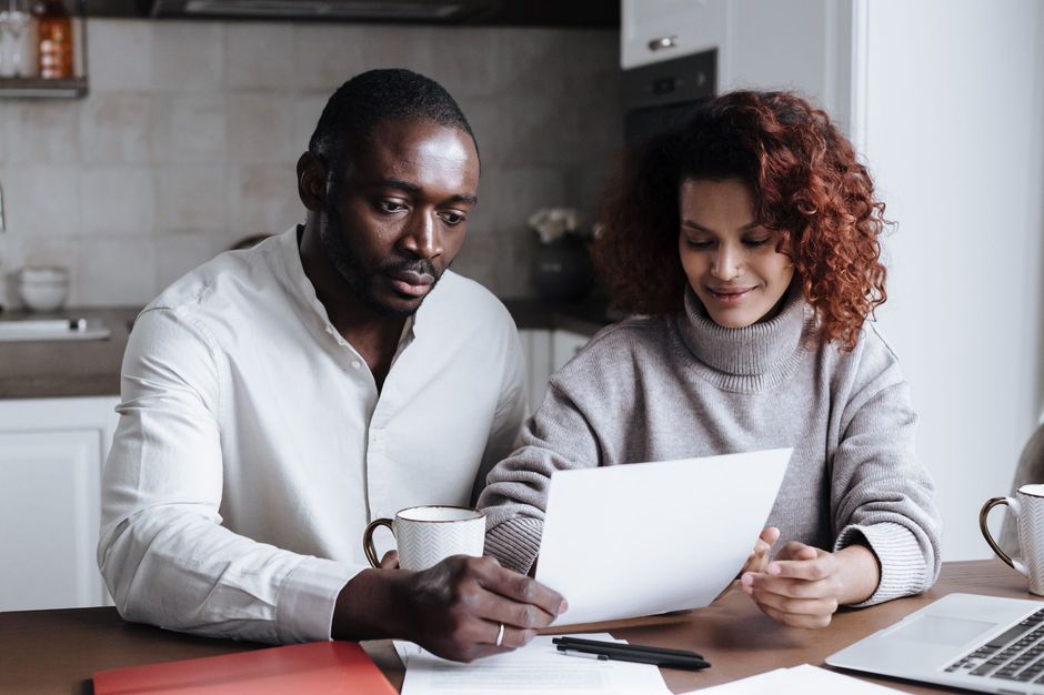 Couple reading a document together at a home table with a laptop